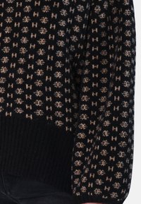 Tröja med svart bas och ett beige mönster av geometriska former och små accenter. Ribbstickade muddar och fåll ger textur.