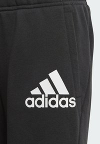 Jogging en coton noir avec un logo Adidas blanc, des éléments de design triangulaires et une texture douce. Comprend des poches latérales.