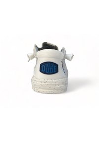 Zapatilla blanca con una superficie texturizada, que presenta un logo azul "HEY DUDE" en la parte trasera y una suela moteada. Incluye una asa y costuras en los laterales.