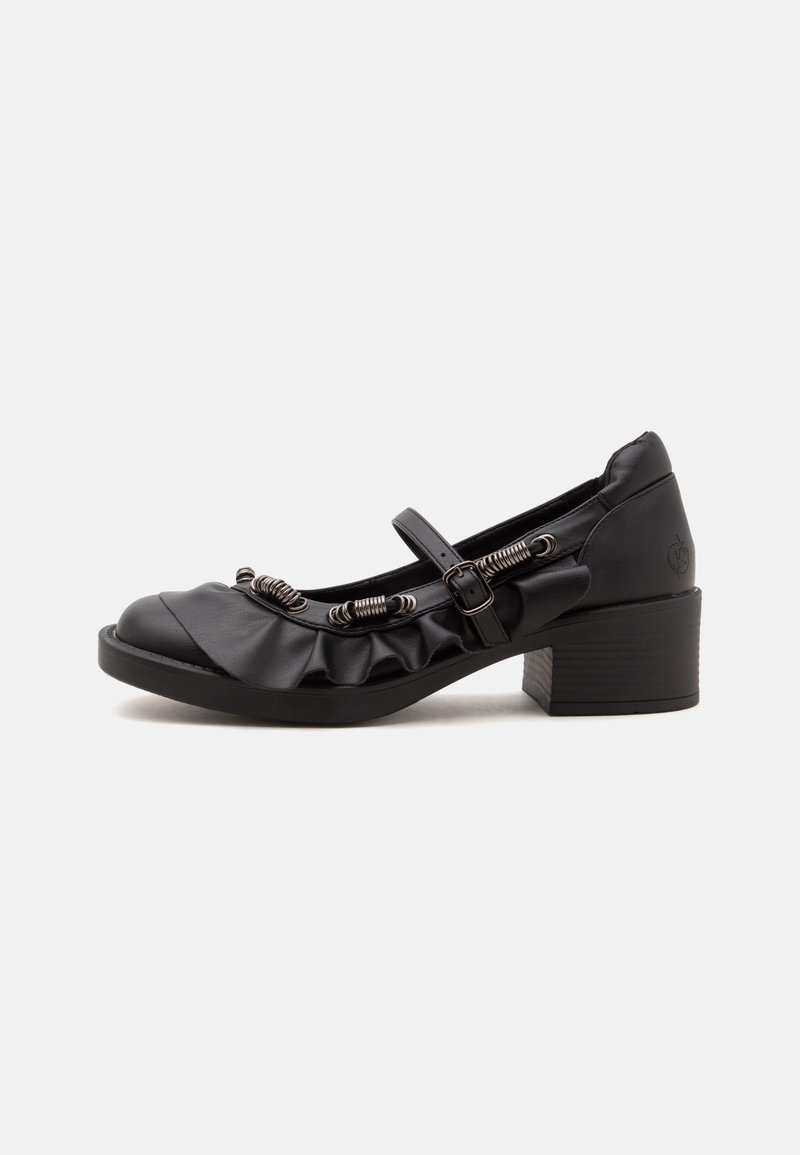 Black low-heeled Mary Jane shoe with ruffled edge, decorative spring coils, and adjustable buckle strap on white background.