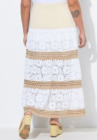 Gonna lunga bianca con sovrapposizione in pizzo, vita in maglia beige e dettagli a righe marroni. Rifinita con un bordo all'uncinetto all'orlo.