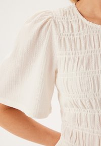 Abito bianco con texture smock, maniche a palloncino corte e corpetto aderente. Il tessuto presenta un motivo a coste sottile.