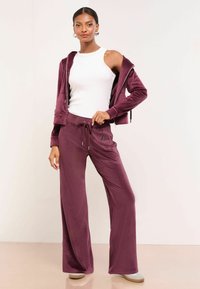 Samtener Trainingsanzug in tiefem Burgunderrot mit einer Jacke mit Reißverschluss und Kapuze sowie passender Jogginghose mit einem "L"-Logo-Akzent.