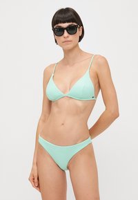 Myntgrønn bikini med ribbet tekstur; trekantet topp med tynne stropper og matchende lavt liv bunn; paret med svarte solbriller.