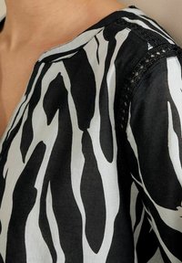 Blusa con stampa a strisce zebrate in bianco e nero, realizzata in un tessuto morbido, con scollatura a V e dettagli in pizzo sulle spalle. Design testurizzato e fluido.