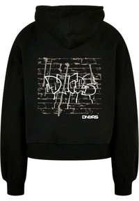 Svart cropped hoodie med huva. Har en grafisk design i vitt som liknar graffiti på en текстurerad bakgrund, med varumärket nederst.