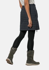 Gequiltede, knielange zwarte rok met een ritssluiting, gecombineerd met zwarte leggings en olijfgroene hoge laarzen met een gesp aan de zijkant.