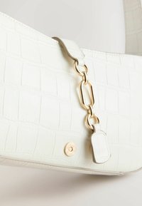 Borsa bianca con texture effetto coccodrillo, dettaglio di catena dorata e chiusura a scatto magnetica su sfondo chiaro.