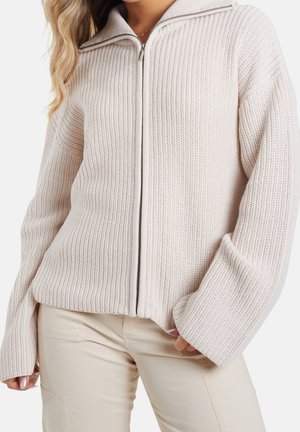 Strikket cremefarvet sweater med høj krave og fuld lynlås, der har en grov tekstur og brede ærmer for en afslappet pasform.