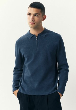 Polo de manga larga azul marino con cuello con cremallera, hecho de un tejido suave con una textura lisa y un ajuste relajado.