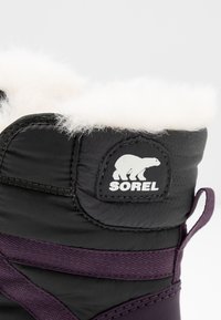 Schwarze und lila isolierte Winterstiefel mit Futter aus Fell, ausgestattet mit einem Sorel-Logo-Patch, strukturiertem Synthetikmaterial und einer Zuglasche.