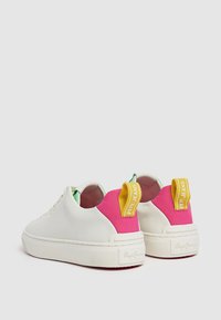 Zapatillas blancas con textura suave, forro interior verde y acentos vibrantes en rosa y amarillo en el talón. Presentan cordones planos y una etiqueta de marca en el talón.