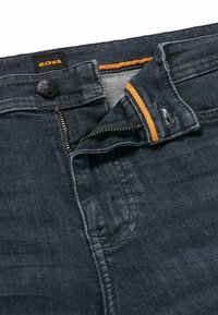 Oöppnade mörka denimjeans med orange trim inuti midjan och en svart knapp märkt "BOSS" på gylfen.