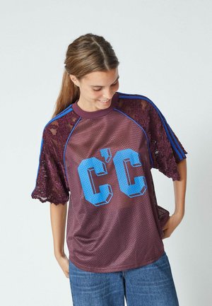 Purple mesh t-shirt with blue striped sleeves and lace accents, featuring a large graphic "C'C" logo in light blue on the front.