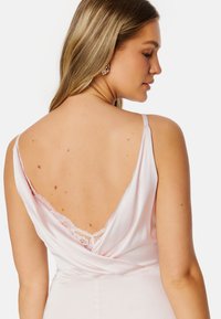 Abito in satin rosa con schiena a barchetta e dettagli in pizzo. Presenta spalline sottili e una silhouette aderente, evidenziando una superficie liscia.