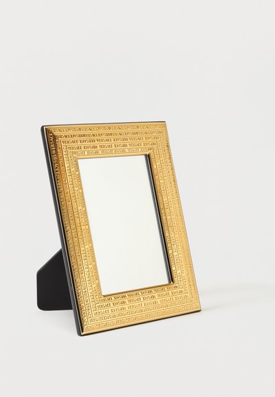 Rama foto dreptunghiulară cu ton auriu, gravată repetitiv cu „Versace”, susținută de un suport negru, înclinat ușor spre stânga pe fundal alb.