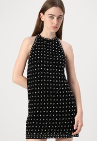 Abito mini senza maniche nero con motivo a diamante, impreziosito da perline argentate, e una silhouette aderente. Tessuto morbido e testurizzato.