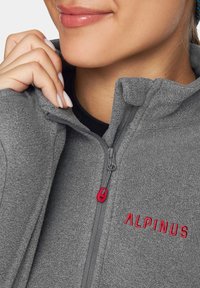 Szara polarowa kurtka z wysokim kołnierzem, z czerwonym haftowanym logiem "ALPINUS" oraz kontrastowymi detalami na suwaku.