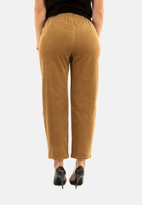 Pantalons en velours côtelé marron avec une coupe ample, présentant un motif texturé et une taille élastique. Associés à des escarpins noirs.