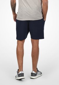 Shorts bleu marine en tissu doux, dotés de poches latérales et d'une coupe décontractée. Associés à des baskets grises avec des accents blancs.