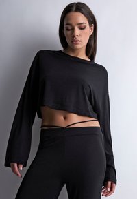 Haut noir à manches longues cropped en tissu doux, associé à des leggings noirs ajustés avec des fines bretelles au niveau de la taille.