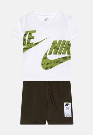 Camiseta blanca de manga corta con logotipos verdes de Nike, combinada con pantalones cortos marrón oscuro, que incluye una etiqueta con el logotipo y las instrucciones de cuidado.