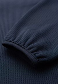 Mörk marinblå långärmad skjorta med en strukturerad yta. Manschettärmar med rynkad tyg för designdetalj. Mjuk, flexibel material.