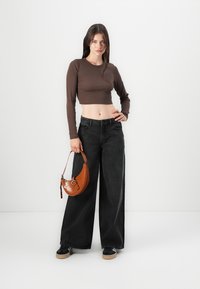 Bruin fit langemouwen crop top gecombineerd met wijde zwarte jeans. Accessoires omvatten een kleine bruin textuur handtas en zwarte sneakers.