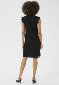 Černé krajkové šaty s krátkými rukávy, vlnitým lemem a květinovým vzorem. Mají výstřih ve tvaru klíče a volný střih, délka po kolena.