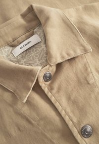 Beige fløjlsjakke med blomstret foret, metalknapper med tryk "GABBA" og mærketikette i kraven.