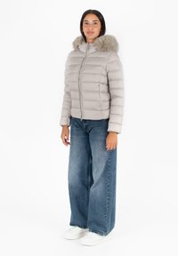 Lichtgrijze pufferjack met een bontgevoerde capuchon, horizontale gestikte stof en een ritssluiting aan de voorkant, gedragen met wijde denim jeans.
