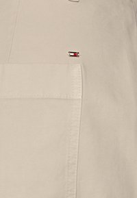 Tissu beige avec une poche rectangulaire cousue et une petite épingle rectangulaire mettant en valeur des blocs de couleurs rouge, blanc, noir et bleu marine.