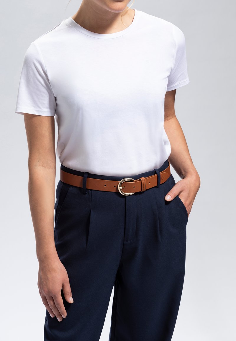 T-shirt blanc à manches courtes associé à un pantalon navy avec des plis à l'avant. Ceinture en cuir marron avec une boucle circulaire en argent.