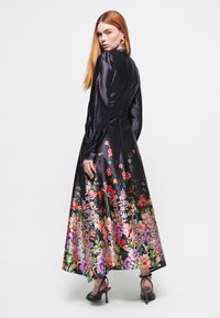 Sort satin kjole med lange pufærmer og blomstermotiver i livlige farver ved kanten, der har en flydende silhuet og elegant detaljer.