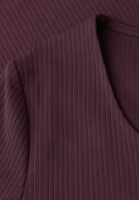 Zbliżenie na prążkowaną tkaninę koloru śliwkowego, ukazujące dekolt w serek oraz krótki rękaw dzianinowego elementu odzieży.