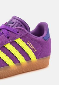 Lila mockaläder sneakers med gula ränder och logotyp. Har en gummisula med strukturerat mönster och en vadderad plös för komfort.