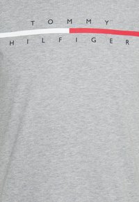 Šedé bavlněné tričko s potiskem loga "TOMMY HILFIGER" a červenými a bílými vodorovnými pruhy na designu.