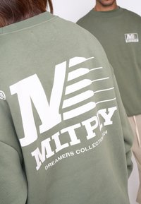 Groene sweatshirt met een groot wit grafisch logo op de achterkant en een kleiner logo op de voorkant, gemaakt van een zachte, gemeleerde stof.