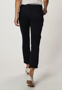 Granatowe spodnie o prostym kroju, z tylnymi kieszeniami z guzikami, podwiniętymi mankietami oraz gładkim, lekko teksturowanym materiałem.