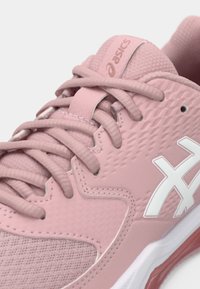 Jasnoróżowy but sportowy z teksturowaną syntetyczną cholewką, wyściełanym kołnierzem, białymi akcentami logo oraz płaskimi sznurowadłami. Posiada elastyczną podeszwę.