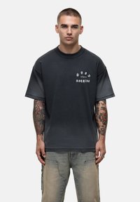 T-shirt noir surdimensionné à manches courtes, présentant un texte graphique blanc sur la poitrine. Le tissu semble doux avec une coupe confortable.