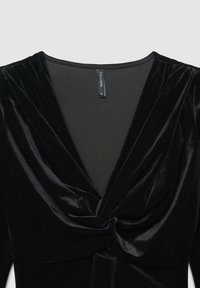 Abito in velluto nero con profondo scollo a V, dettagli plissettati e un accento annodato in vita, dalla texture morbida e dal design elegante.