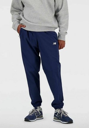 Dunkelblaue Jogginghose mit elastischem Bund und Bündchen, aus leichtem Stoff. Kombiniert mit einem grauen Sweatshirt und graublauen Sneakers.