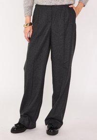 Pantaloni a vita alta di colore grigio scuro realizzati in tessuto testurizzato, con pieghe, tasche laterali e silhouette a gamba ampia. Abbinati a scarpe nere.