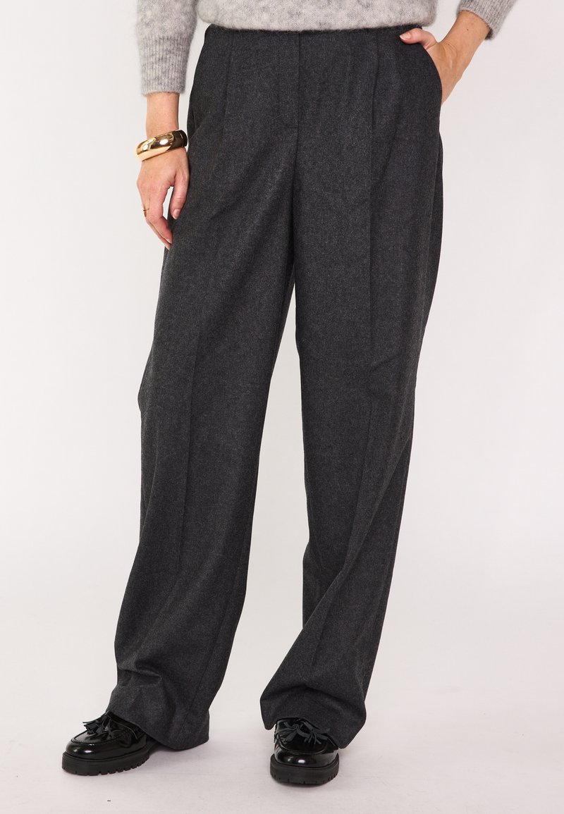 Pantaloni a vita alta di colore grigio scuro realizzati in tessuto testurizzato, con pieghe, tasche laterali e silhouette a gamba ampia. Abbinati a scarpe nere.