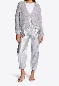 Pastel multicolored knitted cardigan with a loose fit and button closure, paired with shiny silver pleated pants and nude heeled sandals.