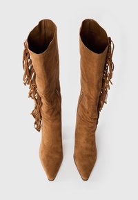 Brown faux suede knee-high boots with pointed toes and side zippers, featuring decorative fringe detailing along outer sides.