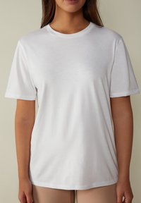 Bílý bavlněný tričko s krátkými rukávy, kulatým výstřihem a hladkým povrchem. Tričko má volný střih a minimalistický design.