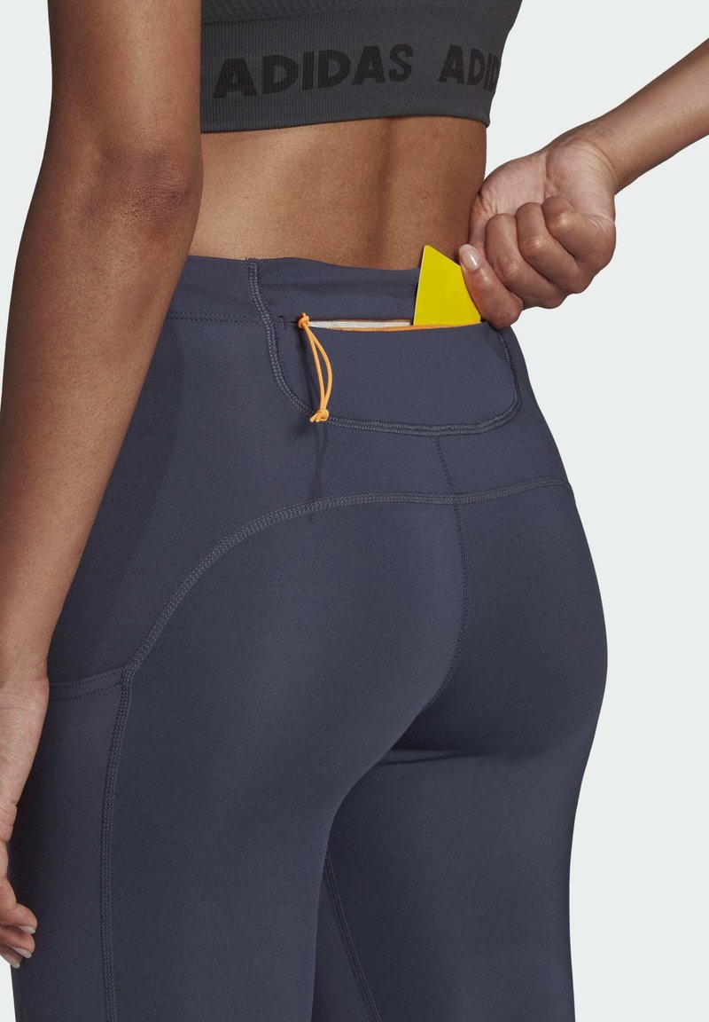 Persoon in donkergrijze Adidas sportkleding steekt een gele kaart in de binnentas met rits van strakke leggings.