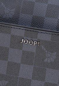 Donkere portemonnee met een geruit patroon, een gestructureerd oppervlak en een metalen "JOOP!"-logo in zilverkleurige afwerking langs de rand.